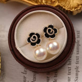 Elegant black and gold flower earrings with pearl drops, perfect imitation jewelry for women. These artificial jewelry earrings feature a black enamel floral design outlined with sparkling cubic zirconia stones, a delicate gold spiral center, and large white pearls for a sophisticated look. Ideal for weddings, parties, and special occasions, these trendy fashion earrings add a touch of luxury to any outfit. A perfect gift for women who love stylish artificial jewelry and statement accessories.