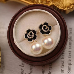 Elegant black and gold flower earrings with pearl drops, perfect imitation jewelry for women. These artificial jewelry earrings feature a black enamel floral design outlined with sparkling cubic zirconia stones, a delicate gold spiral center, and large white pearls for a sophisticated look. Ideal for weddings, parties, and special occasions, these trendy fashion earrings add a touch of luxury to any outfit. A perfect gift for women who love stylish artificial jewelry and statement accessories.